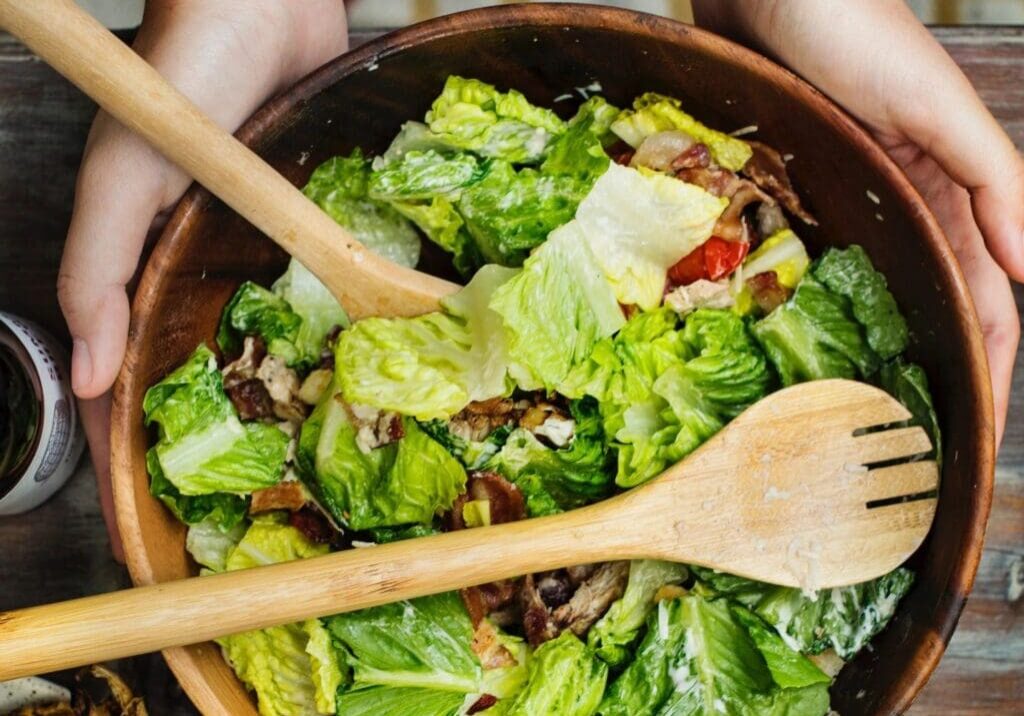 A bowl of salad with wooden utensils in it.