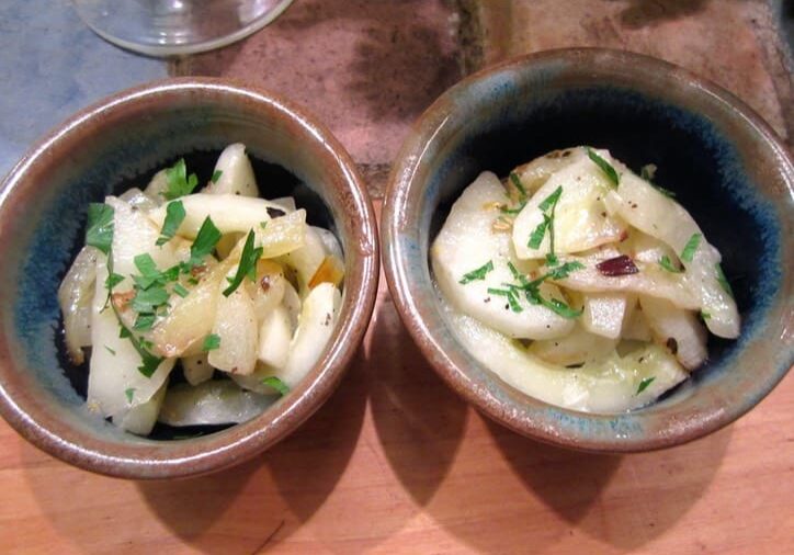 Two bowls of food on a table with wine glasses.