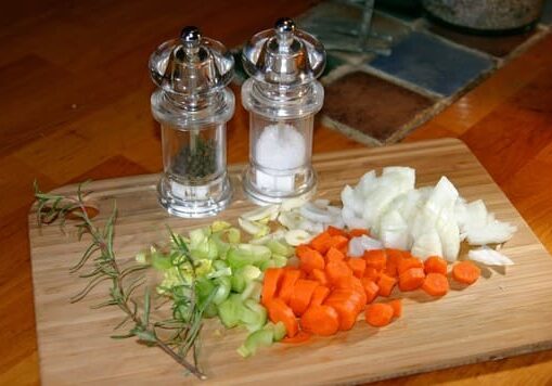 A cutting board with onions, carrots and garlic.