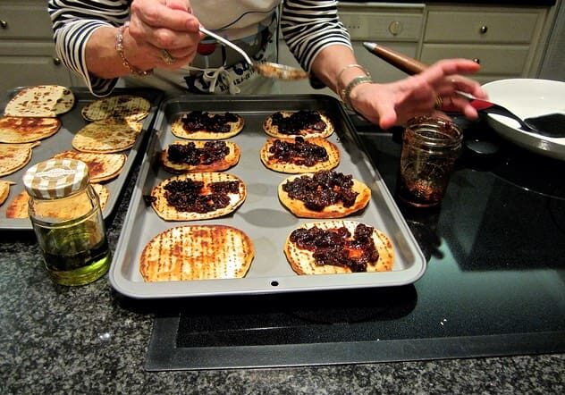 A person is putting toppings on some food.