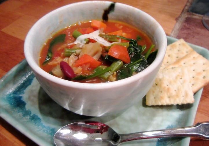 A bowl of soup on a plate with spoon and crackers.