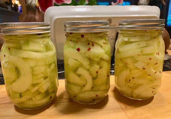 Three jars of pickles sitting on a table.