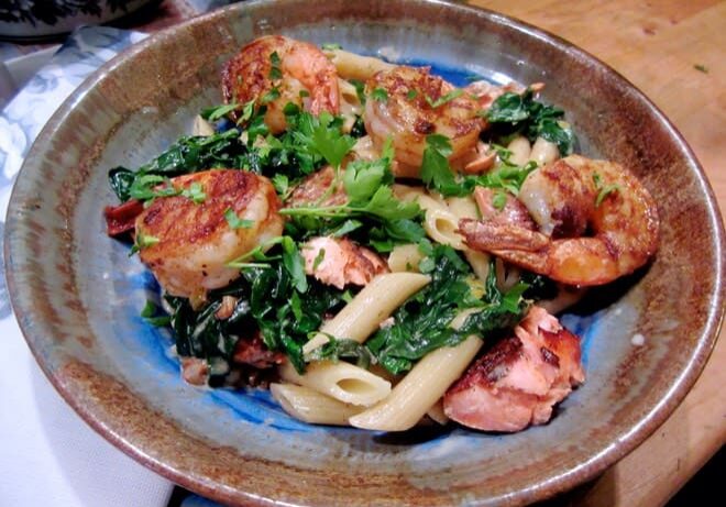 A bowl of pasta with shrimp and greens.