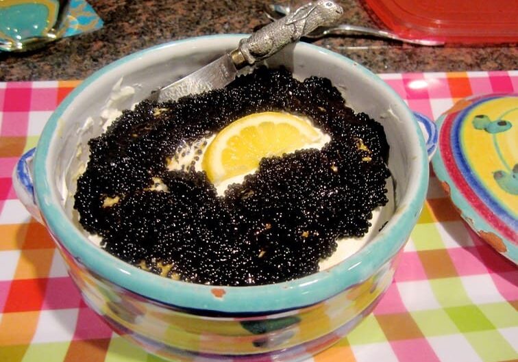 A bowl of black caviar with a lemon slice.