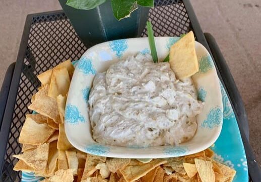 A bowl of dip with chips and a plant on a table.