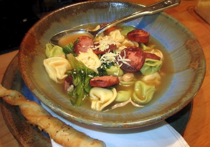 A bowl of tortellini soup with sausage and broccoli.