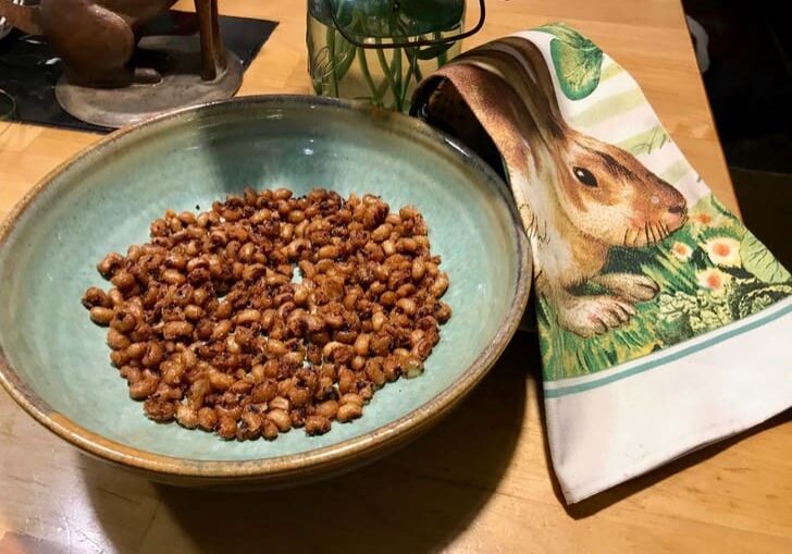 A bowl of peanuts on a table next to a towel.