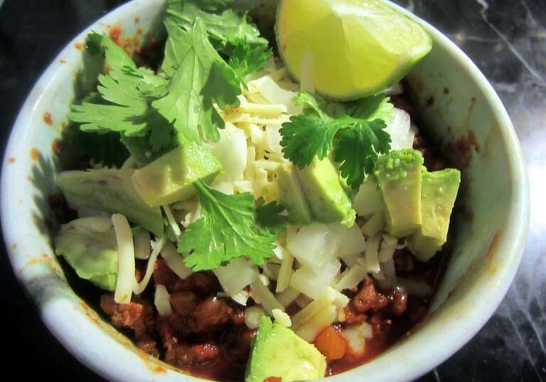 A bowl of food with meat, vegetables and lime.