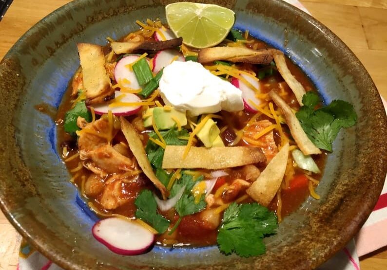 A bowl of food with tortilla strips, cheese and radishes.