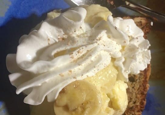 A piece of cake with whipped cream and banana slices on top.