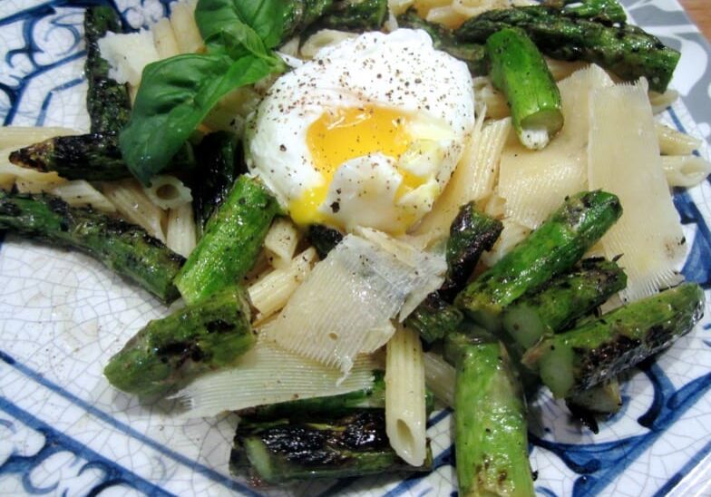 A plate of pasta with asparagus and an egg.