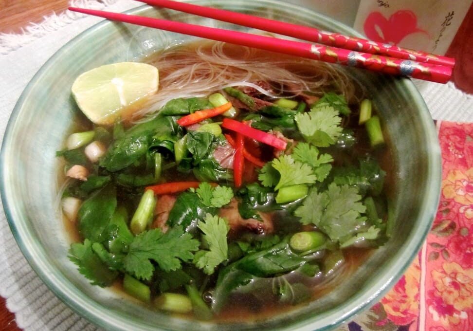 A bowl of soup with chopsticks and lemon.