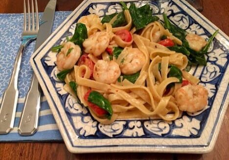A plate of pasta with shrimp and spinach.