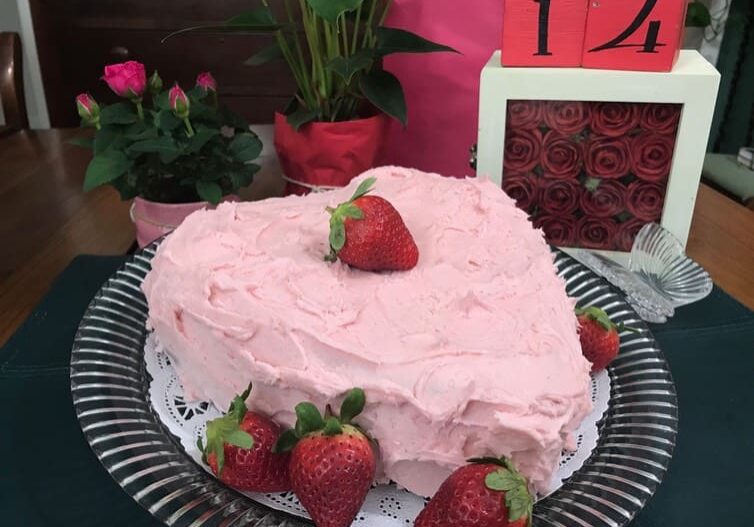 A heart shaped cake with pink frosting and strawberries on top.