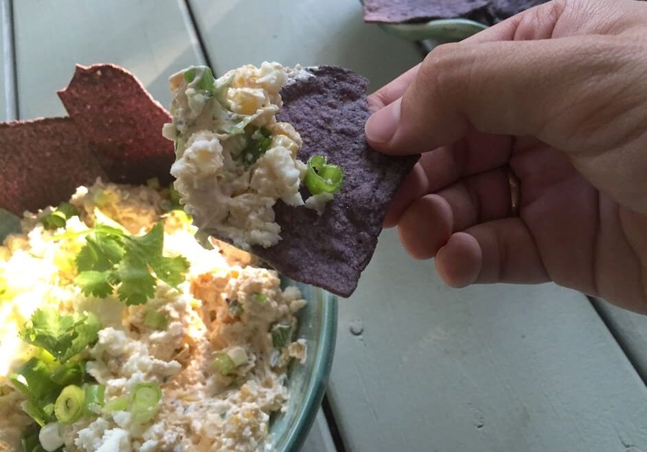 A person holding a tortilla chip over a bowl of rice.