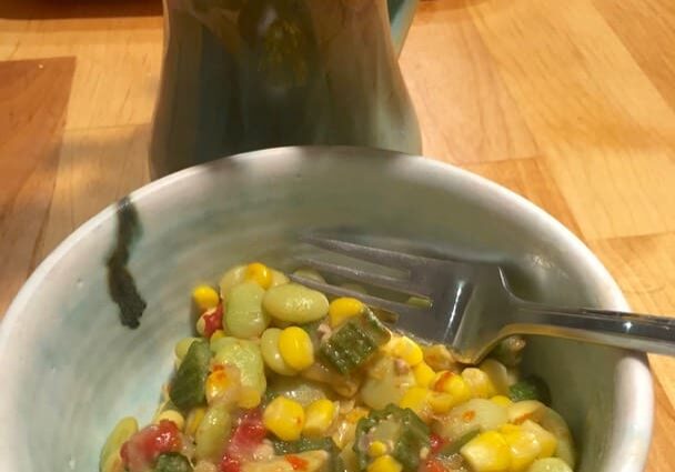 A bowl of corn and zucchini with a fork in it.